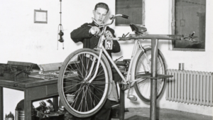 Eine historische Fotografie in einer Fahrradwerkstatt. Fahrrad auf einem Ständer und junger Mann, der repariert