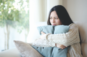 Mädchen umfasst ein Kissen und schaut melancholisch aus dem Fenster